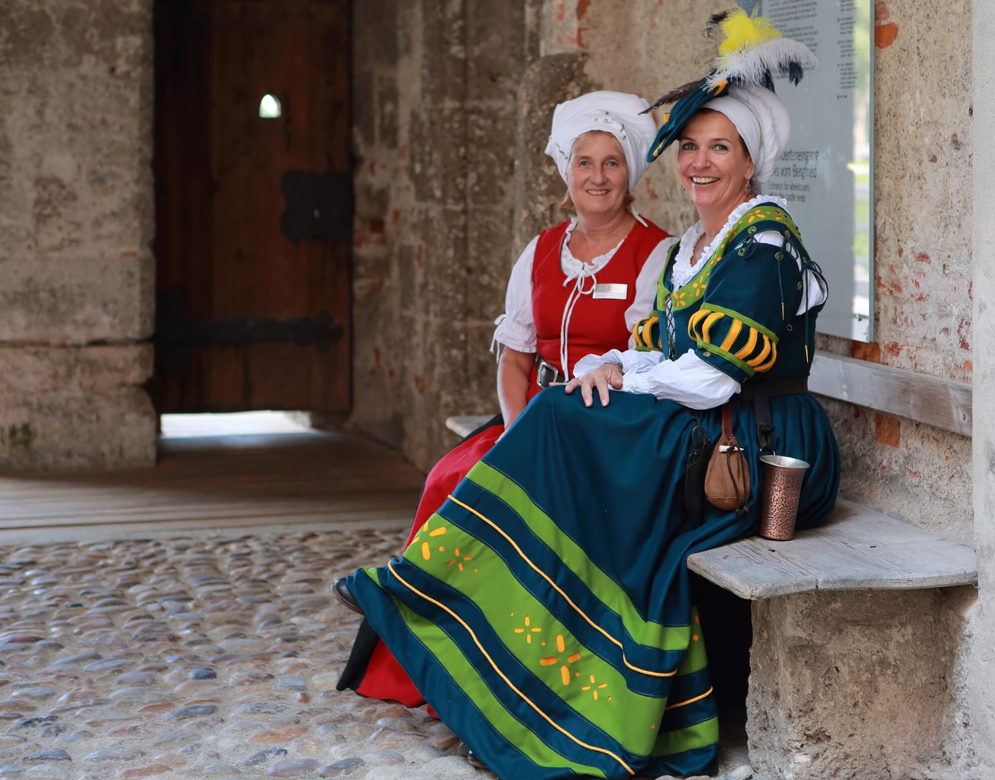 Historisch gewandete Gästeführerinnen auf einer Bank der Burghauser Burg