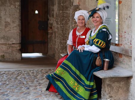 Historisch gewandete Gästeführerinnen auf einer Bank der Burghauser Burg